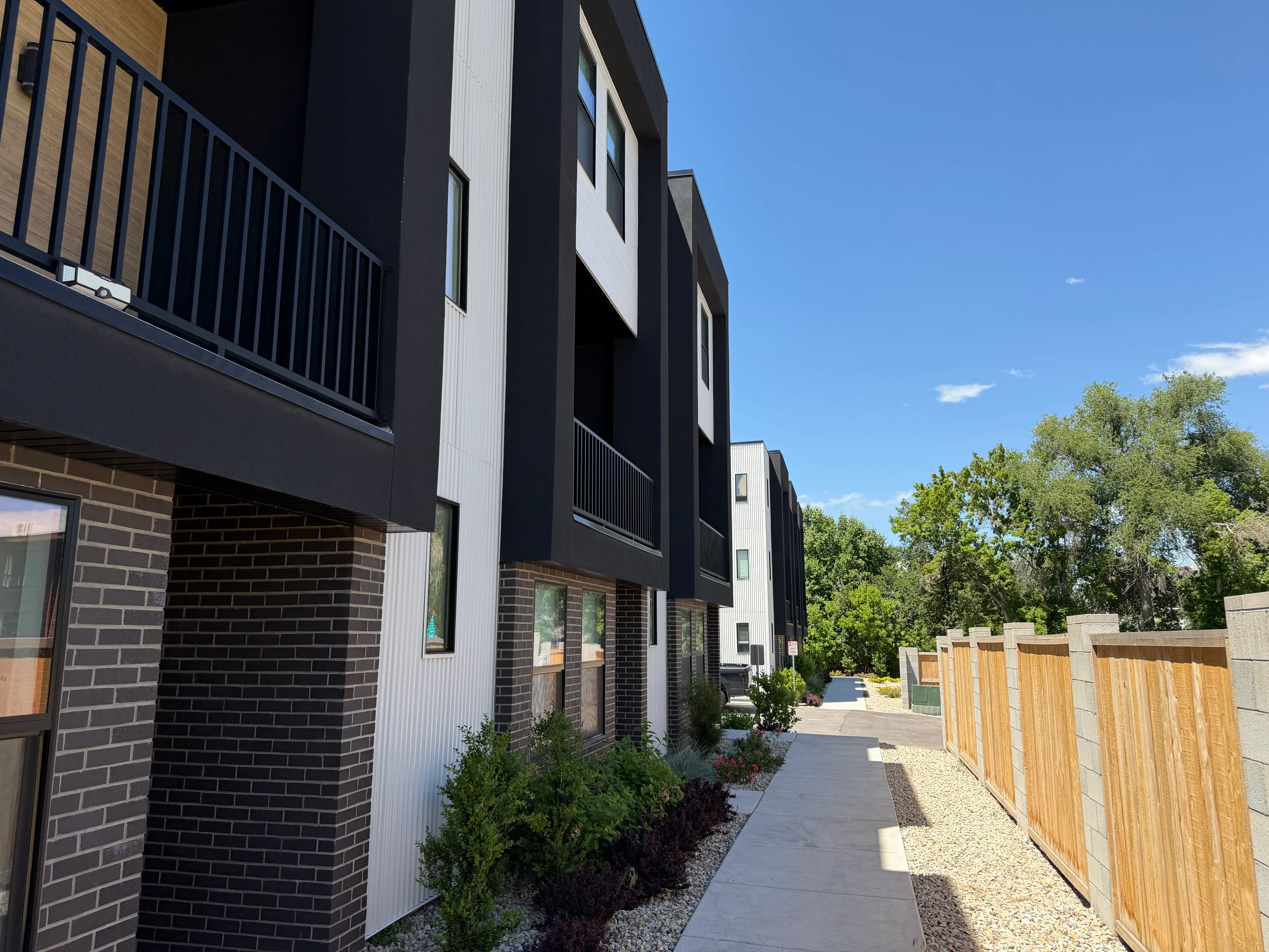 Landscaped walkway alongside the townhomes with fresh plantings, a paved path, and a privacy fence