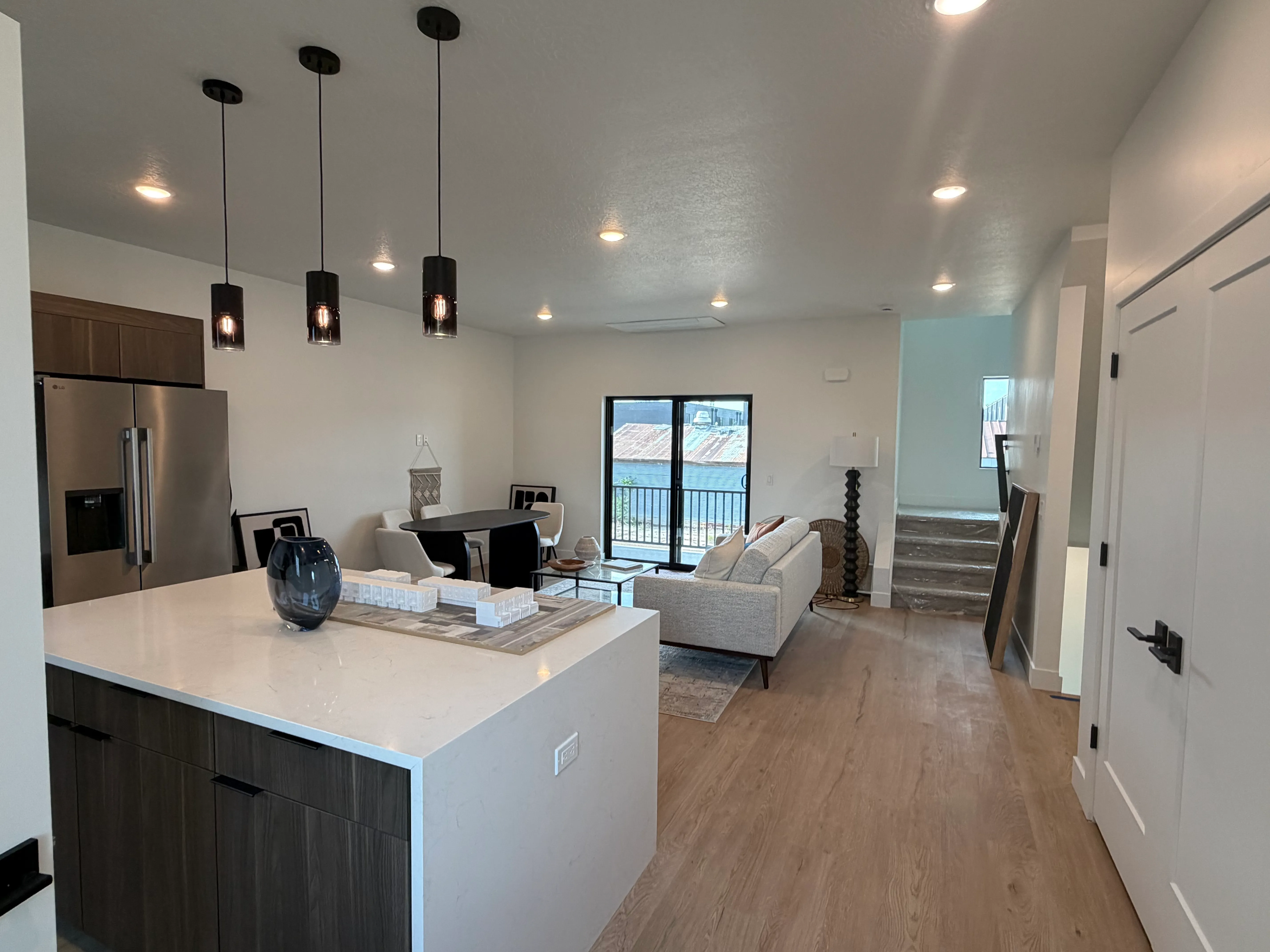 Furnished open-concept main floor: a chef's kitchen with a quartz waterfall island and pendant lights flows into a staged living and dining area with light wood floors
