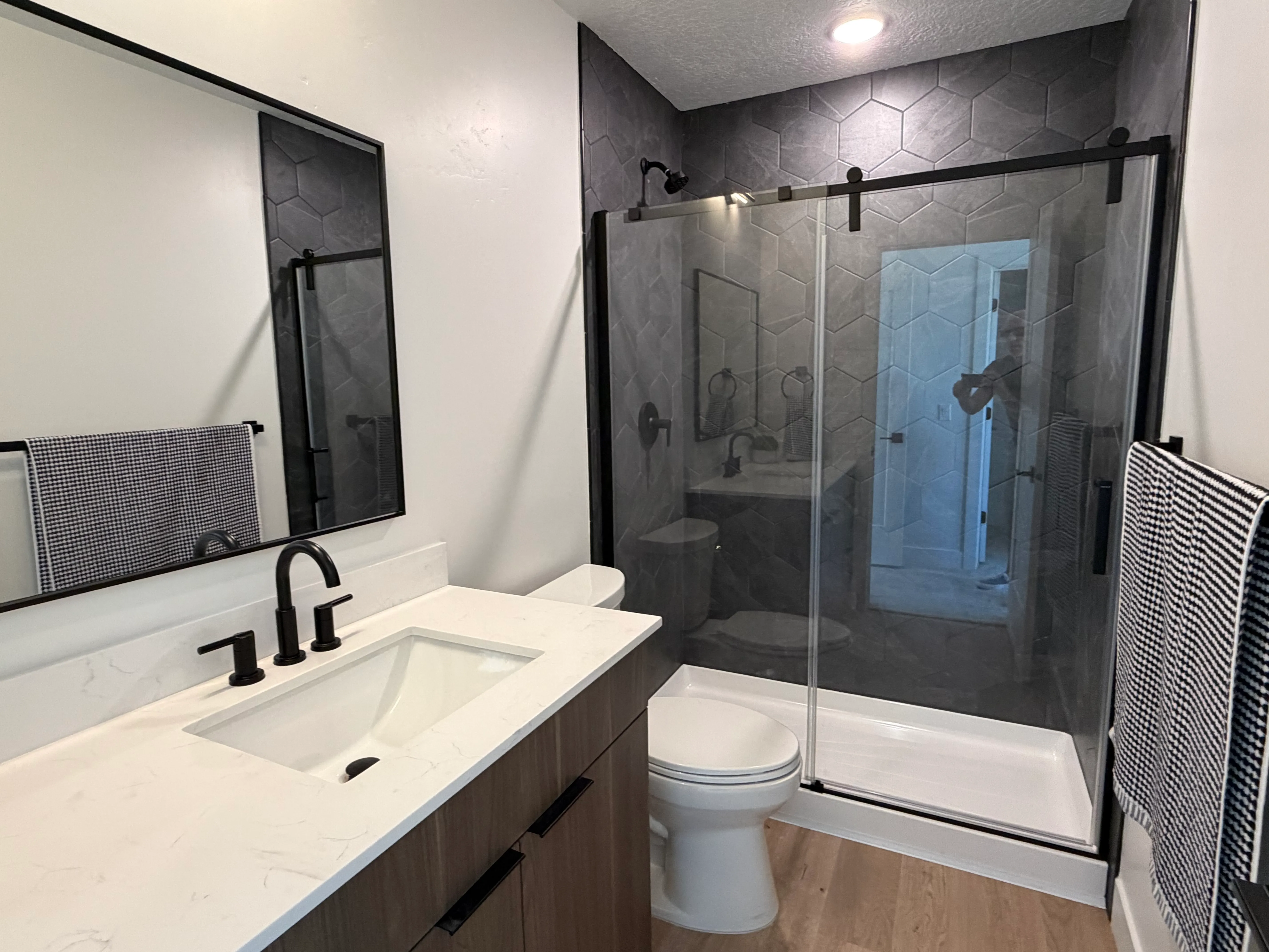Bathroom with a glass walk-in shower, hexagon tile, matte-black fixtures, and a quartz vanity